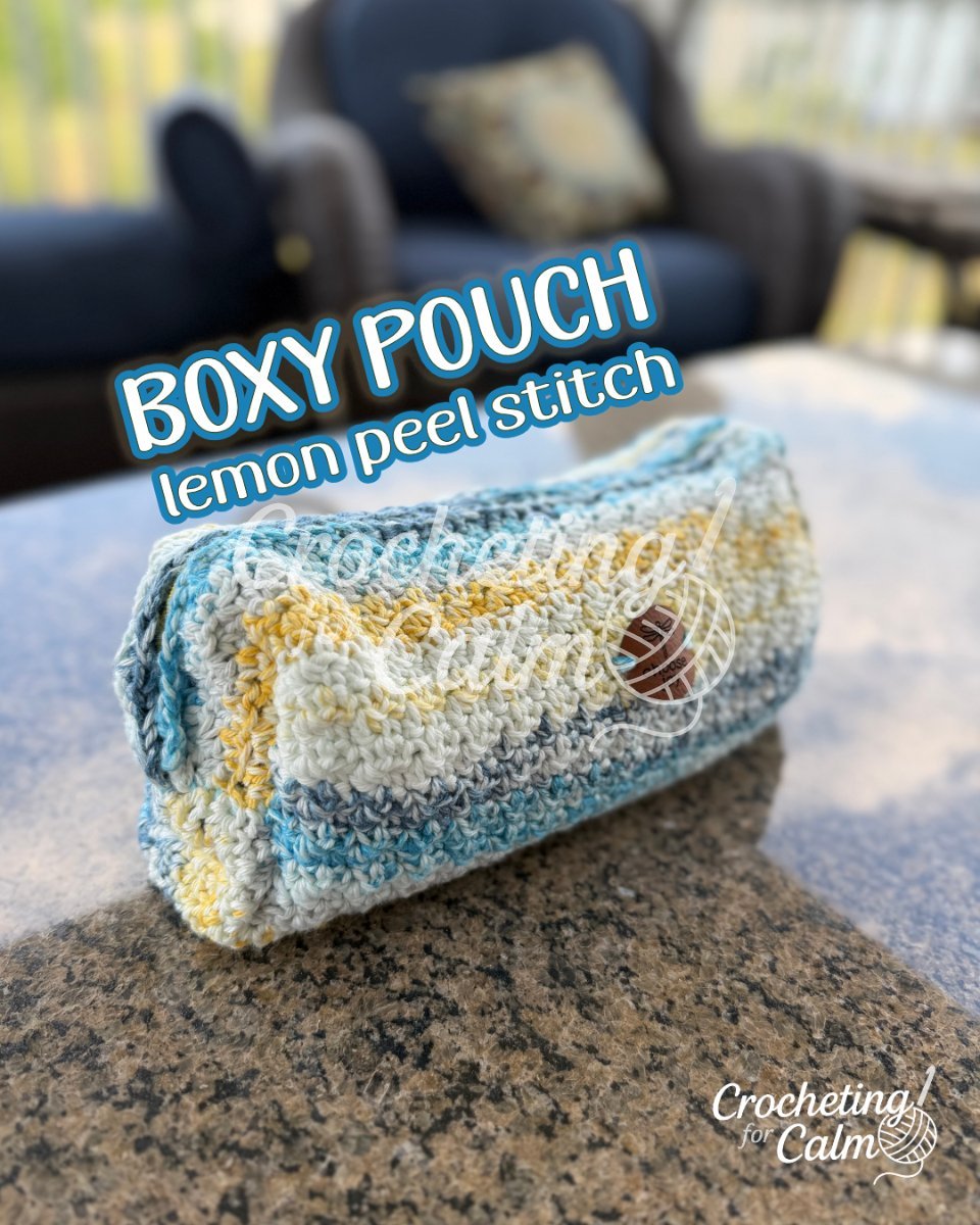 A rectangular boxy crochet pouch worked in a striped lemon peel stitch using variegated blue, cream, and yellow yarn. The pouch rests on an outdoor table with a small leather dragonfly tag that reads "choose joy". Text overlay reads "BOXY POUCH lemon peel stitch" with the Crocheting for Calm logo.