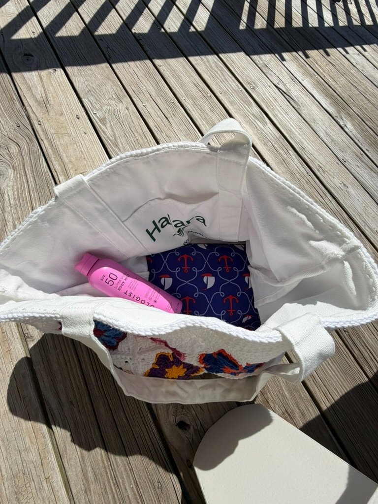 Inside view of a white crochet tote bag lined with a repurposed white canvas Halara bag, showing a pink sunscreen bottle and a blue nautical anchor-print fabric lining the bottom.