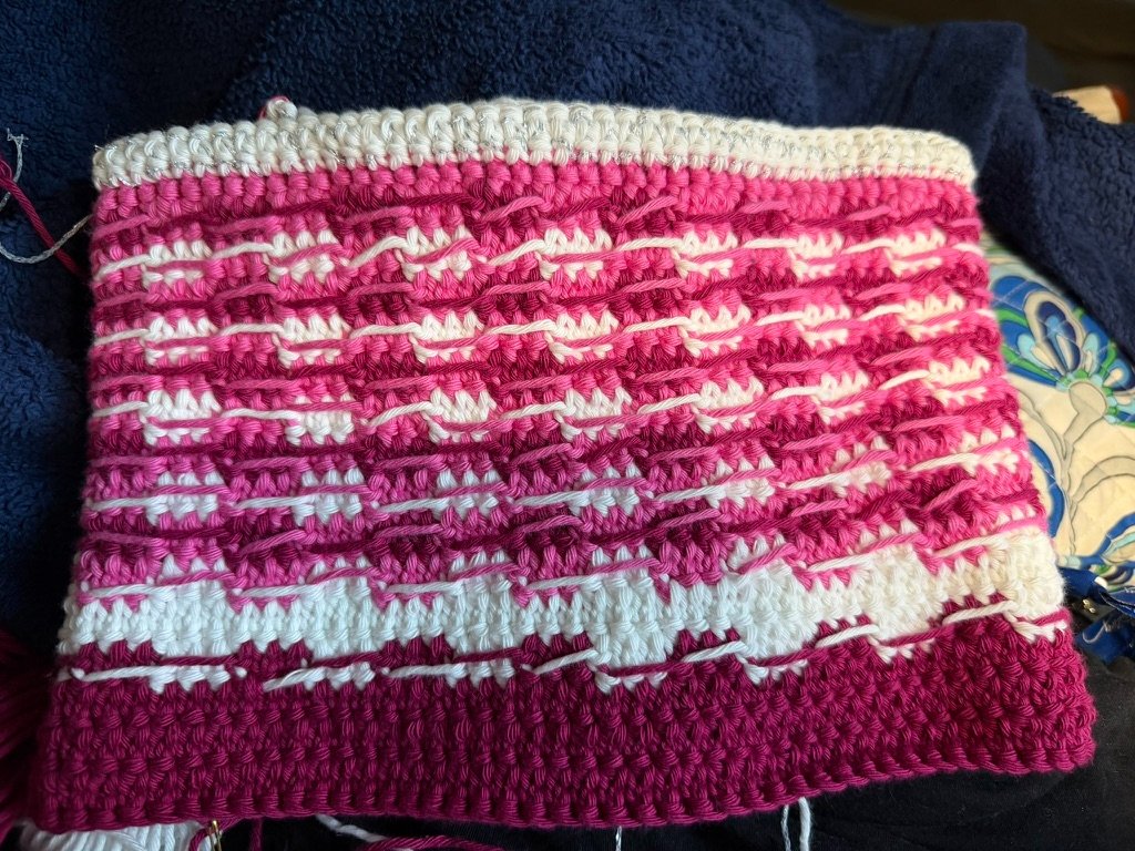 Interior view of a pink, fuchsia, and white crochet pouch project showing carried yarn floating across the back of the stitches instead of being worked inside them.