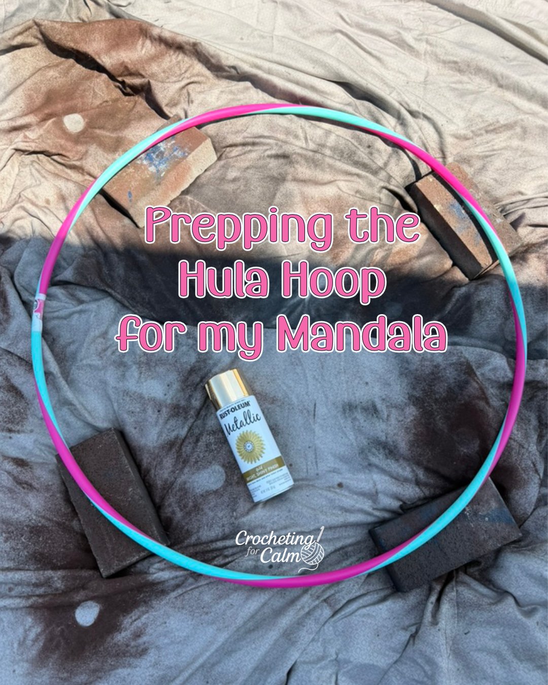 Pink and teal plastic hula hoop being prepped for a crochet mandala project, propped up on four bricks on a drop cloth with a can of gold metallic spray paint in the center and text overlay that reads "Prepping the Hula Hoop for my Mandala."