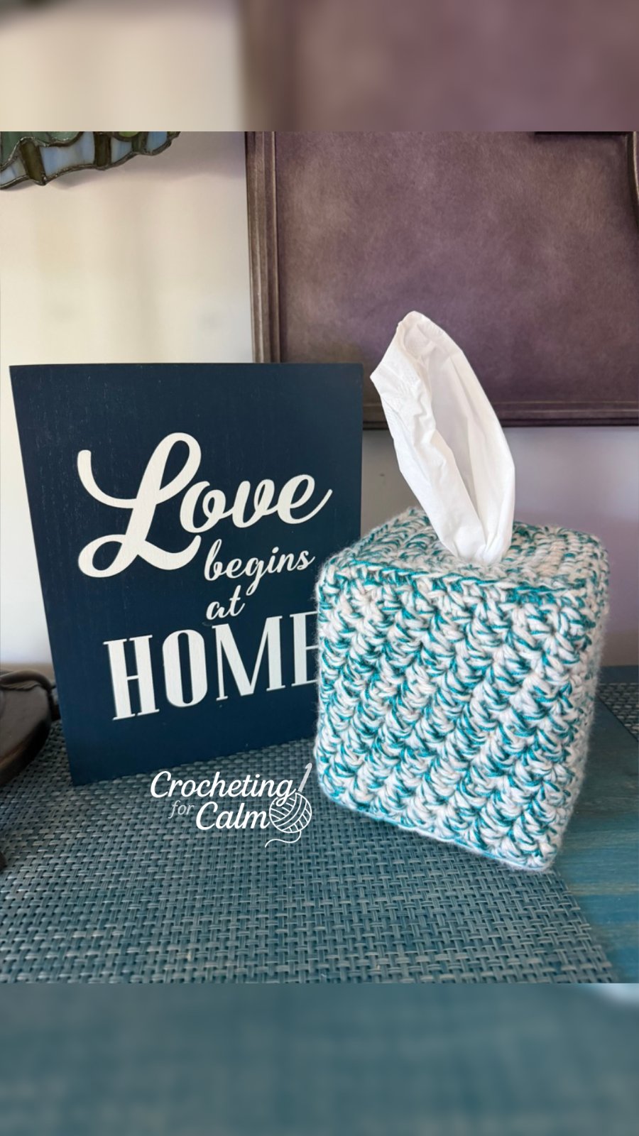 Neutral cream and teal square tissue box cover with a textured crochet stitched pattern, resting on a tabletop.