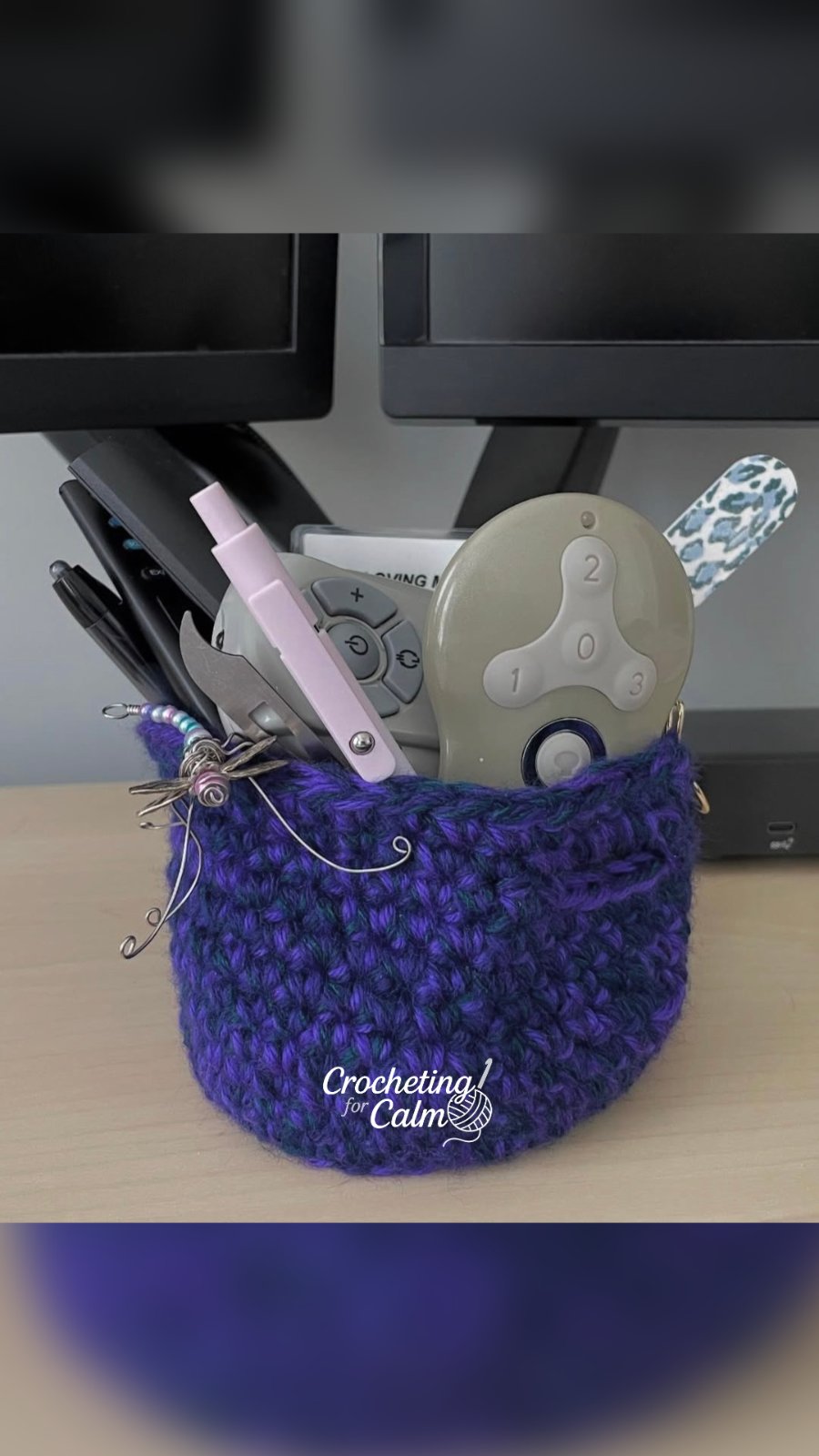 Navy and purple small desk basket crocheted and stuffed with desk accessories. Small dragonfly hanging off the edge.