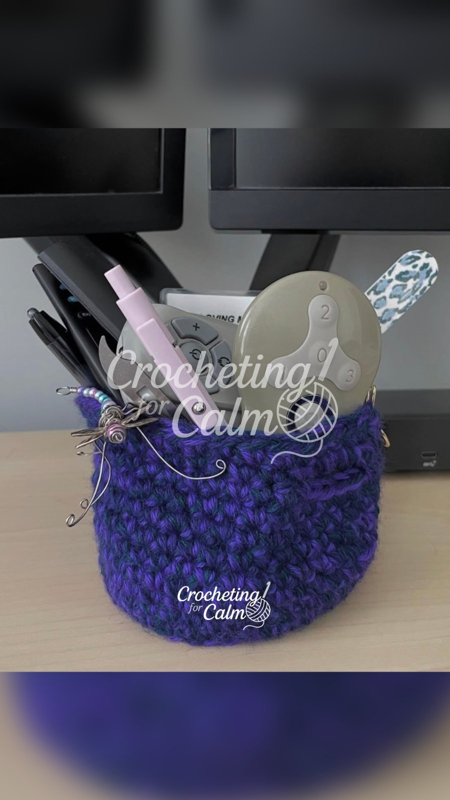 Navy and purple small desk basket crocheted and stuffed with desk accessories. Small dragonfly hanging off the edge.