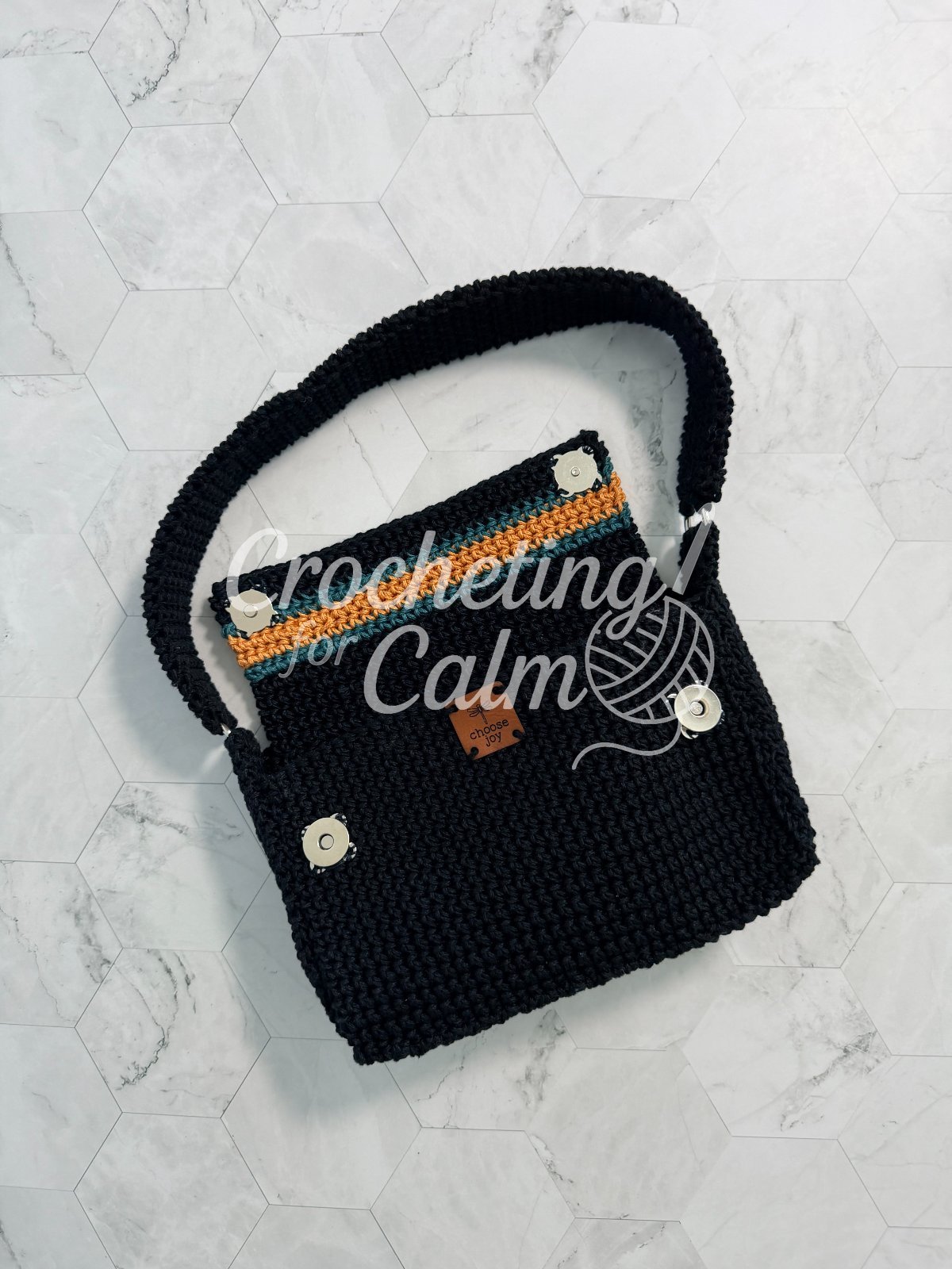 Interior and hardware view of an open black crochet shoulder bag on a marble tile surface, showing silver magnetic snap closures, a top flap with teal and gold stripes, and a center logo tag.