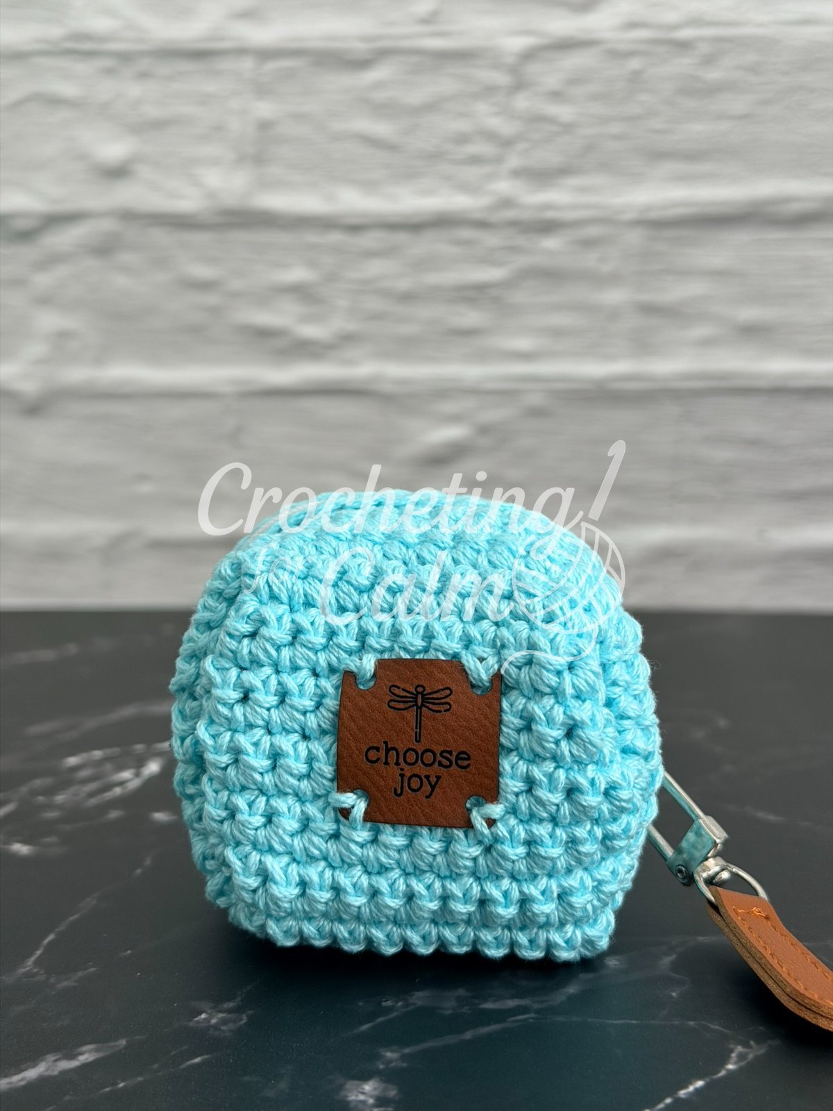 Tiny Zippered Crocheted Cube Pouch in teal yarn sitting on a marble countertab. A tag with "Choose Hope" and a leather zipper pull.