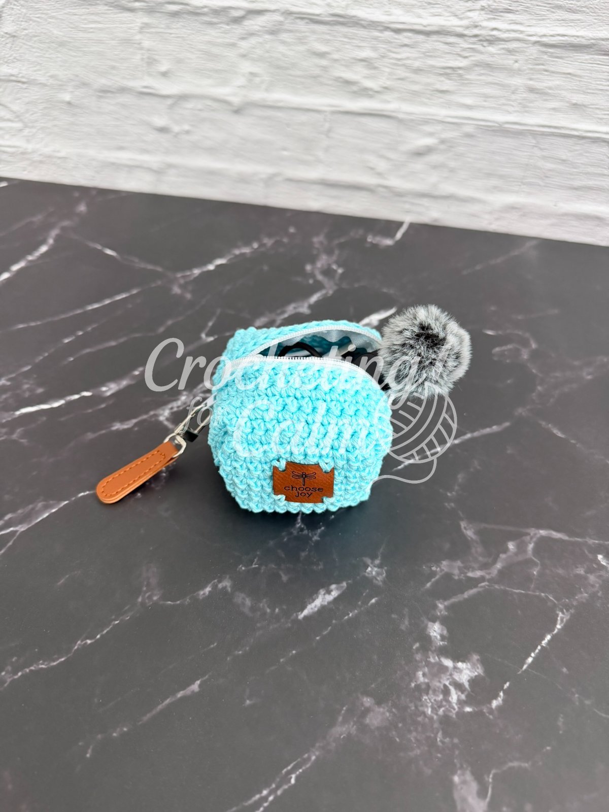 Tiny Zippered Crocheted Cube Pouch in teal yarn sitting on a marble countertab. A tag with "Choose Hope" and a leather zipper pull. A microphone poking out of the pouch.