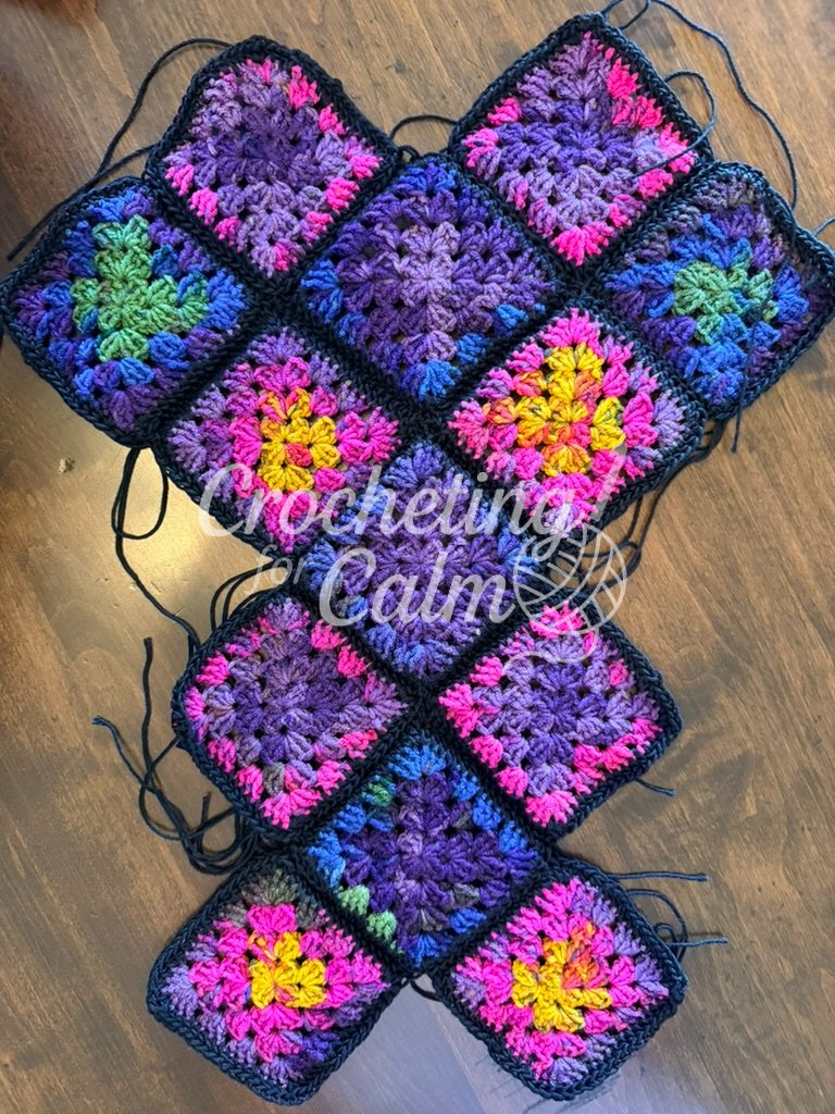 Close-up flat lay of colorful granny square panels joined together with black 3-weight yarn, showing the layout before shaping into a 13 square tote.