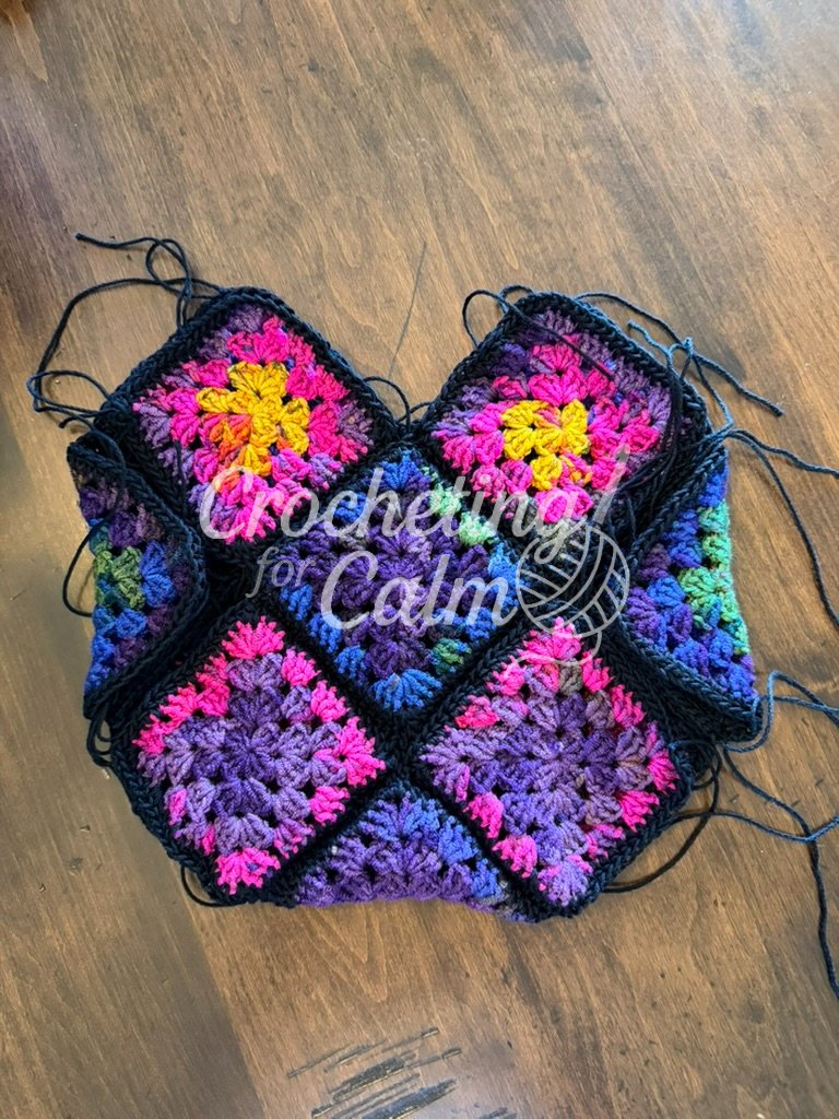 Colorful granny square panels joined together with black 3-weight yarn, showing the layout after folding but before stitching together for a 13 square tote bag.