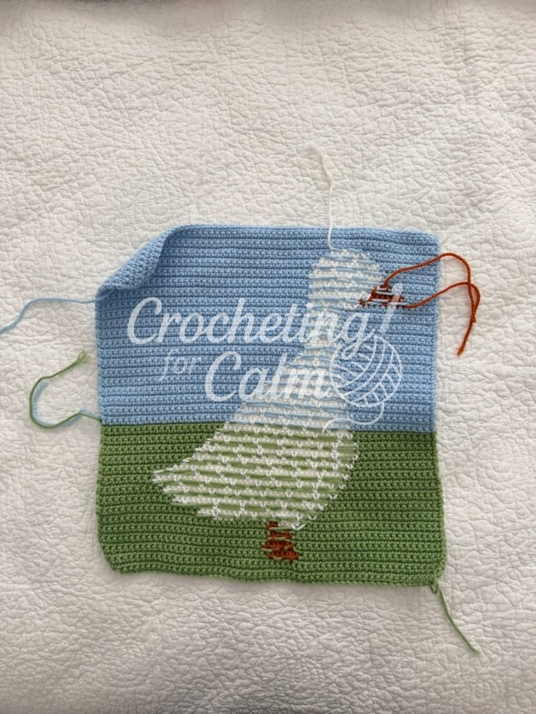 The reverse side of the tapestry crochet duck panel laid flat on a white background, showing the carried yarn floats and color transitions across the green field and blue sky.