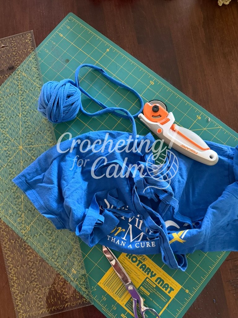 A shirt sitting on a green cutting mat with a rotary cutter. T-shirt being made into t-shirt yarn